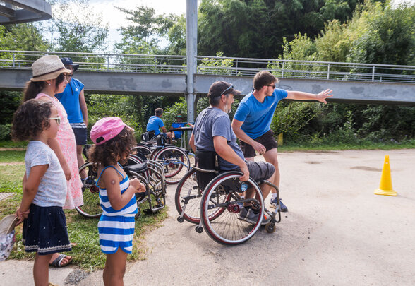 Activité handisport en fauteuil roulant en plein air, encadrée par un animateur, avec des enfants et adultes participants - Agrandir l'image, fenêtre modale