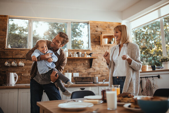 Parents et jeune enfant partageant un moment de joie dans une cuisine lumineuse au décor chaleureux. - Agrandir l'image, fenêtre modale