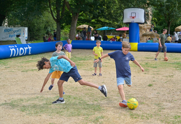 Enfants jouant au football en plein air lors de Niort Plage, avec un panier de basket gonflable en arrière-plan - Agrandir l'image, fenêtre modale