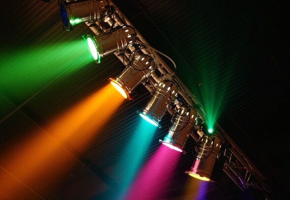 Projecteurs de scène colorés suspendus à une structure, diffusant des faisceaux lumineux vert, orange, cyan et rose - Agrandir l'image, fenêtre modale