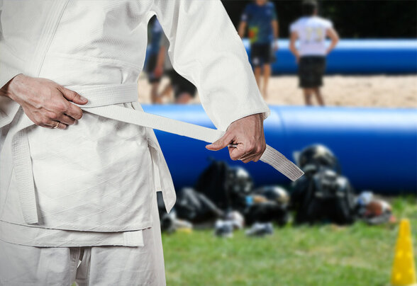 Pratiquant d'hapkido en kimono blanc nouant sa ceinture blanche, structure gonflable bleue en arrière-plan - Agrandir l'image, fenêtre modale