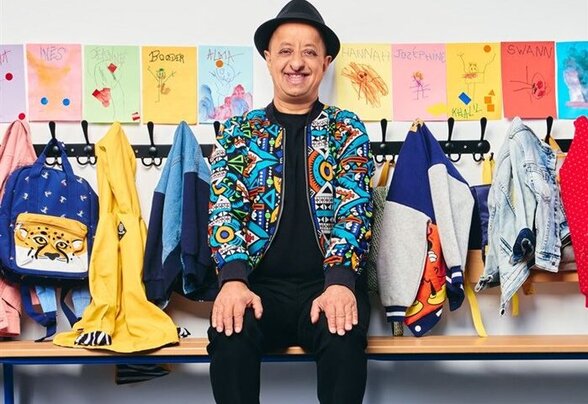 Affiche du spectacle : Booder assis sur un banc dans un vestiaire d'école, entouré de cartables colorés et de dessins d'enfants - Agrandir l'image, fenêtre modale