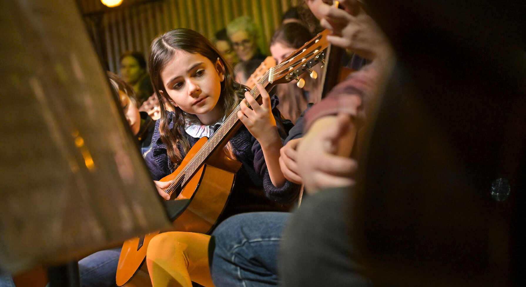 Jeunes élèves jouant de la guitare classique en groupe lors d'un concert, pupitre à partitions au premier plan